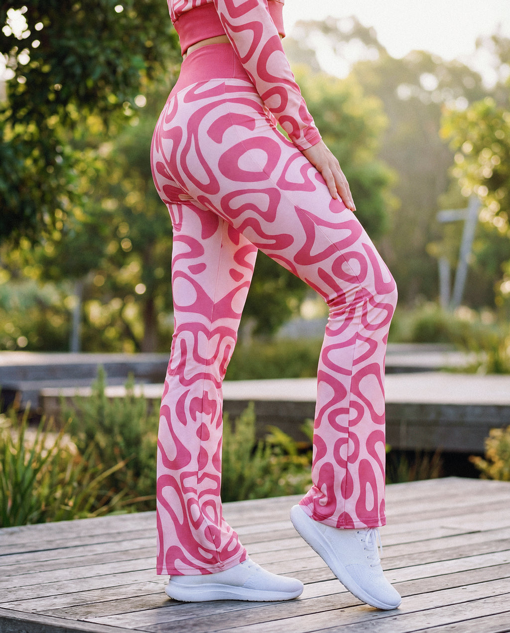 Person wearing pink patterned leggings standing on a wooden deck with greenery in the background