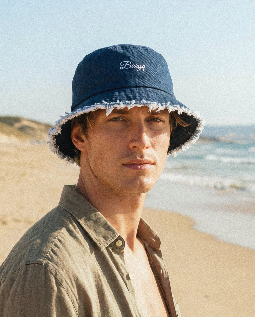 Man wearing a navy bucket hat with 'Barry' embroidery on a beach.