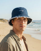 Man wearing a navy bucket hat with 'Barry' embroidery on a beach.