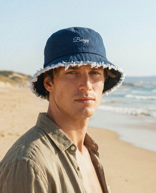 Man wearing a navy bucket hat with 'Barry' embroidery on a beach.