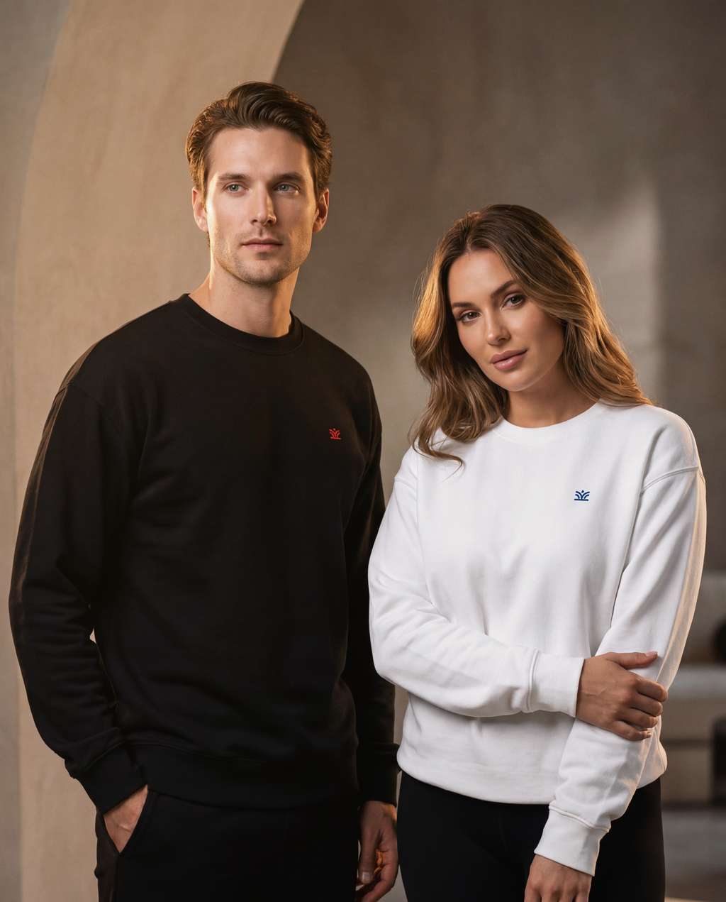 Two people wearing black and white sweatshirts standing against a neutral background
