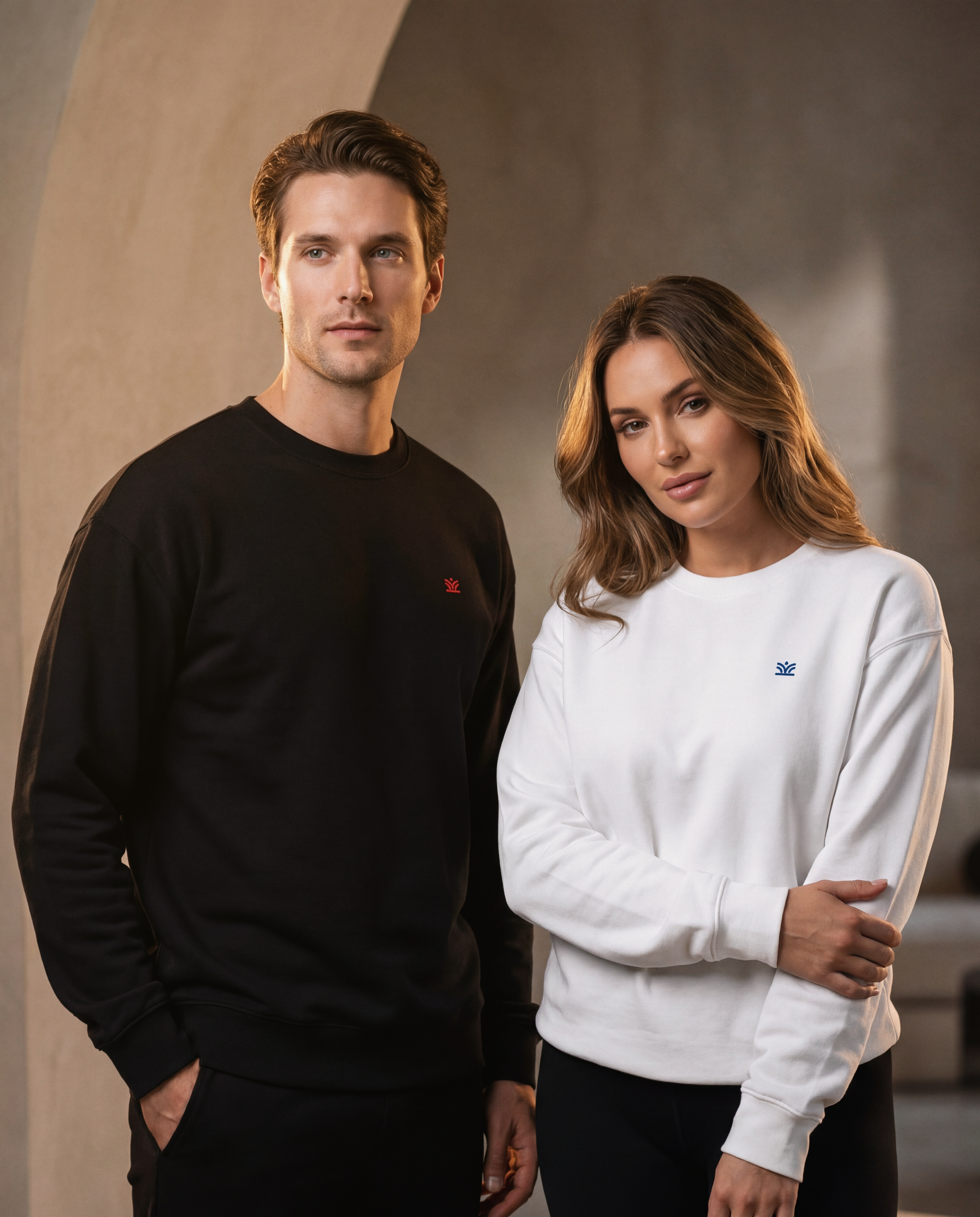 Two people wearing black and white sweatshirts standing against a neutral background