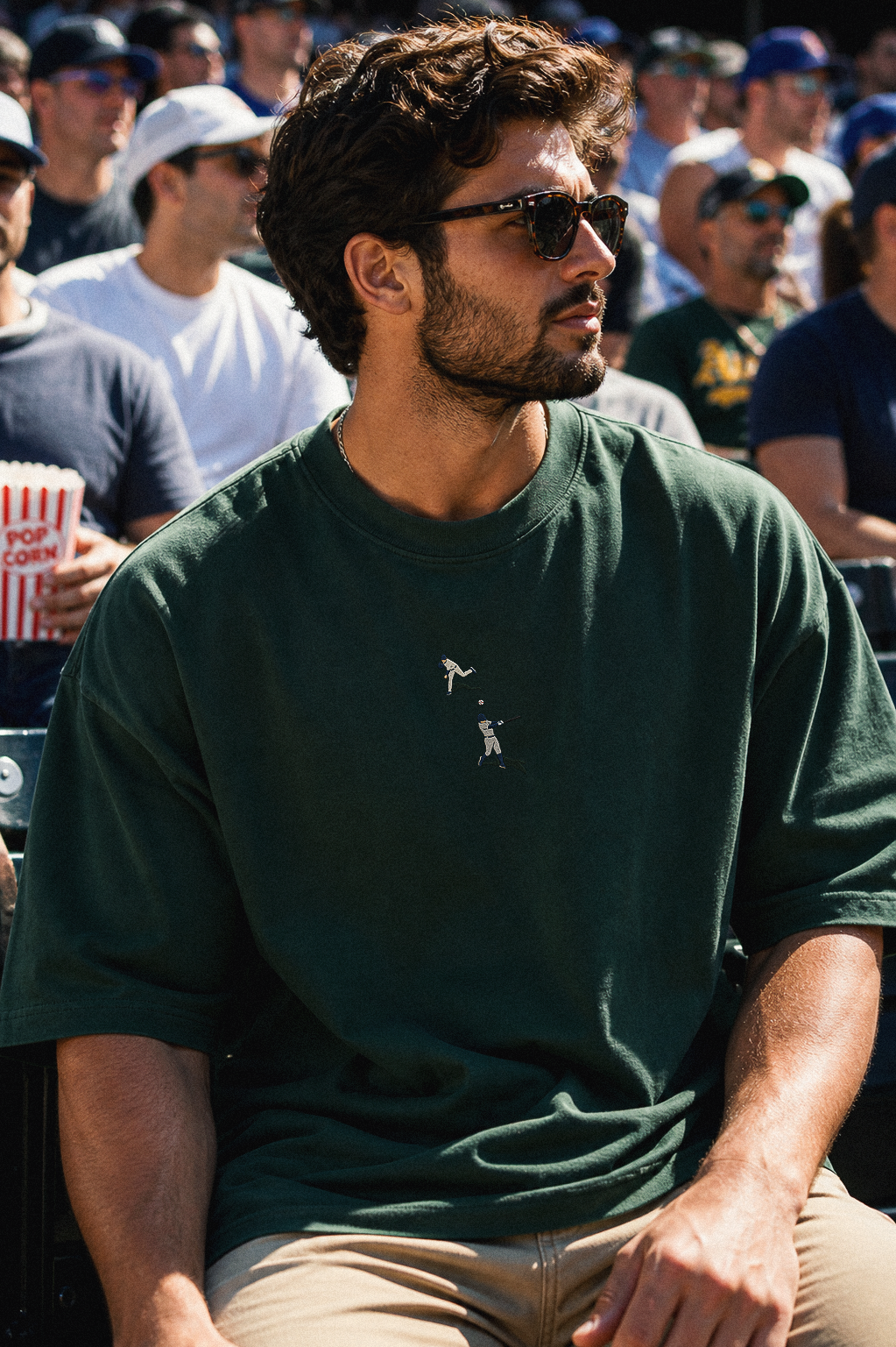 Man wearing sunglasses and a green t-shirt sitting among a crowd.